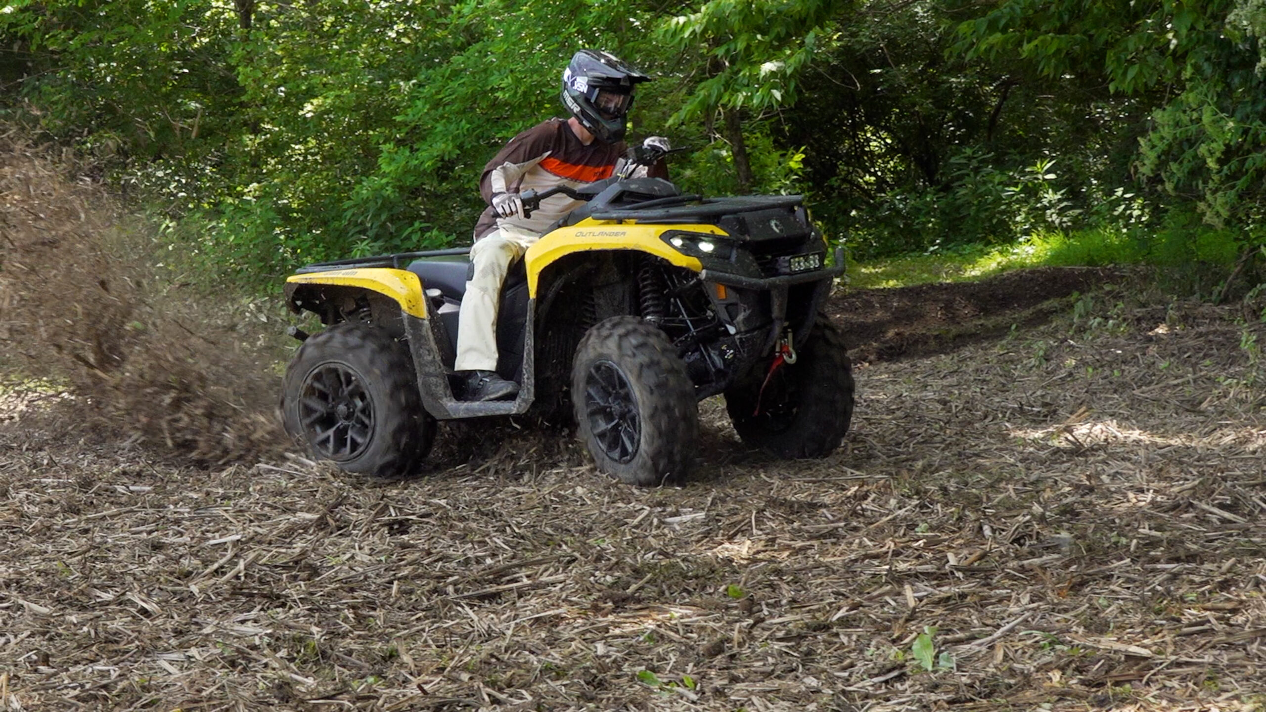 Checking. Outlander 700 coming at the camera, three-quarter front view, drifting through a mulched corner.Okay, we're almost done here. Quick question
